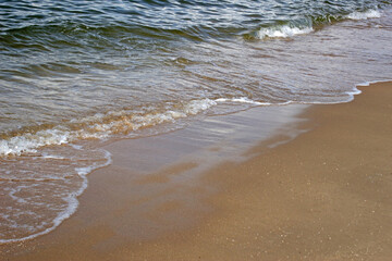 Gentle waves from green colored ocean shallows reaching a sandy beach