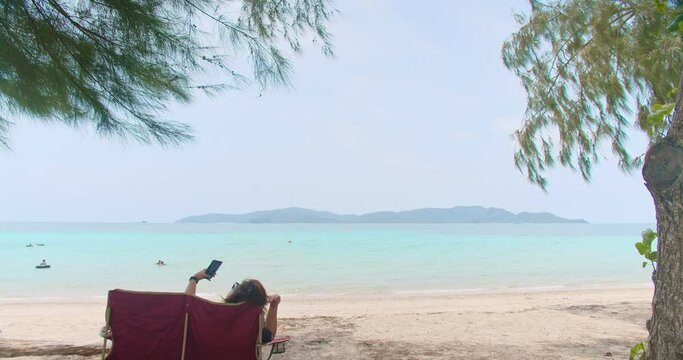 young Asian tourist woman sitting on beach chair relaxing enjoy vacation holiday weekend at beautiful tropical sor beach in sunny day summer time at Sattahip, Thailand