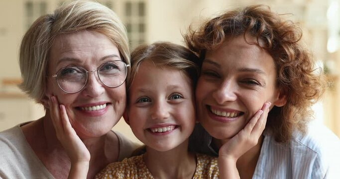 Three generations of relatives beautiful women, multi-generational family close up portrait concept, cute girl grandkid posing between 60s granny and loving mother smiling for camera laughs feel happy