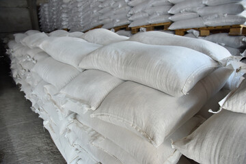 Bags of grain and flour are placed on wooden pallets in straight rows in the warehouse of the processing plant.
