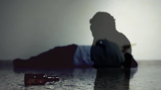 The silhouette of a desperate man, projected over the body of the same person lying on the floor, drunk or dead. Dramatic shot.
