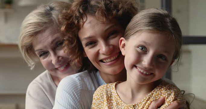 Multi generational family close up portrait concept. Little girl her young mother and elderly grandmother hugging sit indoor laughing having fun enjoy priceless time together, feeling love and tender