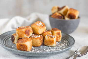 Square curd pancakes, traditional Russian cheese cakes in a gray plate and bowl, with coconut flakes. Selective focus.
