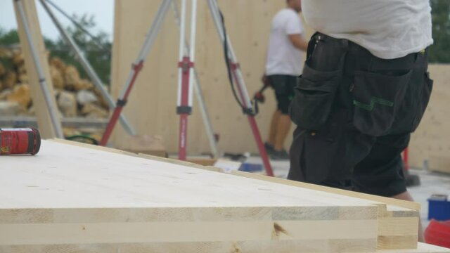SLOW MOTION, CLOSE UP, DOF: Unrecognizable male builder picks up a CLT beam from a workbench at an unfinished housing project. Contractor carries a glued laminated board across construction site