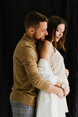 Beautiful young pregnant woman and man hugging and kissing in the studio.