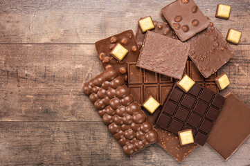 Composition bars and pieces of different milk and dark chocolate, on rustic wooden background. Milk chocolate chunks. top view, Assorted chocolate making a frame with copy space