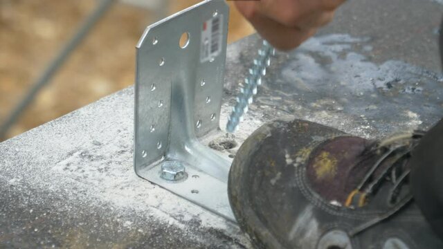 SLOW MOTION, CLOSE UP, DOF: Unrecognizable builder uses a power drill to fasten a bolt into bitumen covered concrete foundation. Contractor fastens a stainless steel wall carrier into the ground.