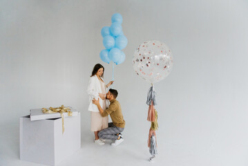 A beautiful young pregnant woman and a man hug and kiss near the box with the inscription boy or girl and balloons. Gender party. Baby shower. 