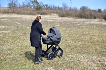 A woman dressed in a black coat on a walk with a baby carriage in the spring nature