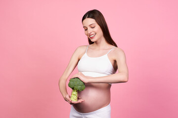 A cute gentle pregnant girl in white clothes with broccoli in her hands.