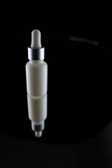 a cosmetic bottle with an eyedropper on a black background is reflected from a mirror surface