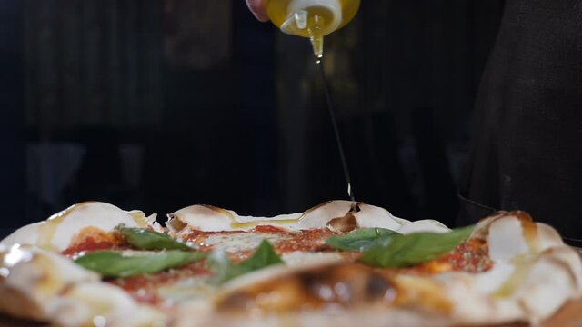 Pouring adding olive oil to ready handhmade pizza. Traditional Italian pizza. cheese and basil. pizza with tomato sause and mozzarella, traditional food in italy, high kitchen gastrobar restaurant