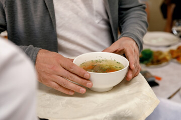 adult man holding a white bowl of chicken soup