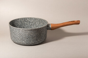 Stone saucepan with wooden handle on solid background.