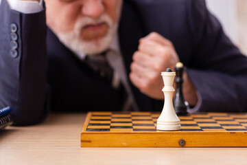 Old male employee playing chess at workplace