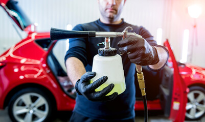 A car service worker cleans interiror with a special foam generator