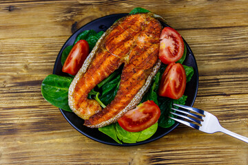 Grilled salmon steak with spinach and tomatoes on wooden table. Top view