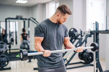 Naklejka na ściany i meble Athletic physical man training in the fitness gym. Strong handsome male working with sport equipment.