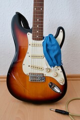 Naklejka premium Blue mask hanging on an electric guitar, leaning against the wall, with a jack cable on the floor, medical mask for protection from all kinds of diseases
