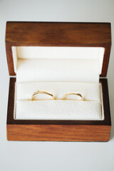 Golden wedding rings in wooden box. Shiny jewelry in gift box on white table. Vertical love symbol background. Marriage jewelry before ceremony.