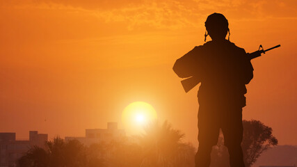 Fototapeta na wymiar Silhouette Of A Solider Saluting Against coastal town . Concept - protection, patriotism, honor.
