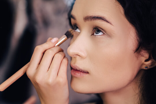Make up talanted artist doing maquillage to woman applying concealer. Visagist using brushes shadows facial professional cosmetics for makeup. Beauty industry studio, image with copy space.
