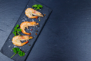 Big raw red prawns with parsley, salt and pepper on a slate board on black background. Top view, copy space