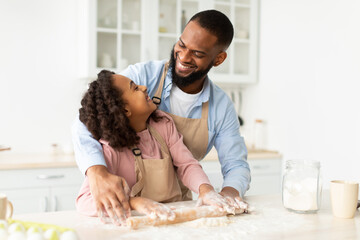 Cheerful black man and his child daughter kneading dough