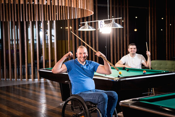 Adult men with disabilities in a wheelchair play billiards in the club