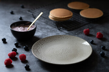 pancakes lie on a grid on a rustic concrete background with yogutz in a pot with golden spoon berries lie on the background