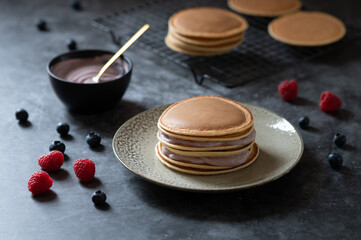 fresh pancakes on a stoneware plate on rustic concrete background with yogurt in a pot with golden spoon berries lying on the background