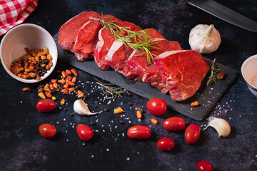 Raw beef meat steaks for grilling with herbs and spices on dark rustic board.