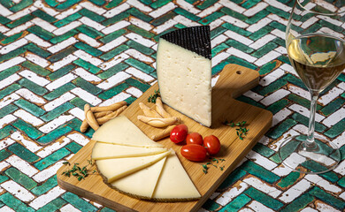 Spanish Manchego cheese sliced with some cherry tomatoes and a glass of white wine over a green and white table.