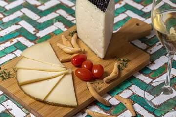 Spanish Manchego cheese sliced with some cherry tomatoes and a glass of white wine over a green and white table.