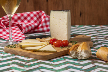 Spanish Manchego cheese sliced with some cherry tomatoes and a glass of white wine over a green and white table.