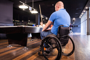 Adult men with disabilities in a wheelchair play billiards in the club