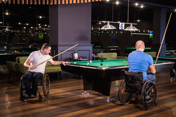 Adult men with disabilities in a wheelchair play billiards in the club