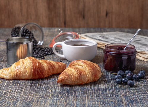 Breakfast with croissants, marmalade and coffee with a newspaper on the background.