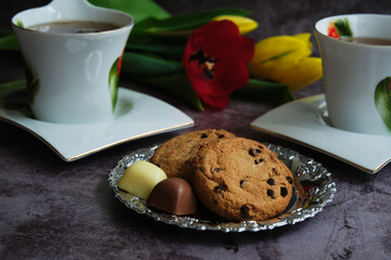 two white cups of tea and yellow and red tulips