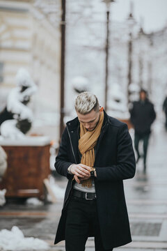 Handsome Young Man In A Black Winter Outfit With A Brown Scarf Checking His Watch While Walking