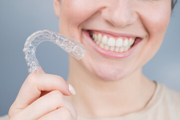 Close-up portrait of a woman holding a plastic transparent retainer. A girl corrects a bite with...