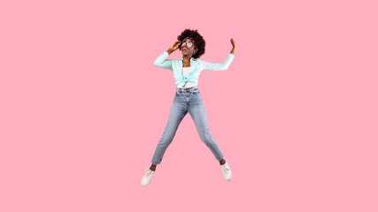 Fototapeta na wymiar Joyful African Woman Jumping Wearing Sunglasses Posing Over Pink Background