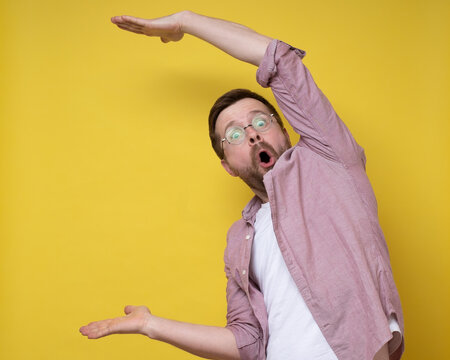 Surprised man in glasses shows a large size with hands, he exaggerates and looks at the camera in amazement. Copy space. 