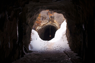 Dark tunnel carved in the rock, surrounded by white snow. Crossing to the other side of the mountain. Exploration, trekking.