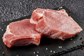 two pieces of raw pork meat with a bone for a steak on a black stone background