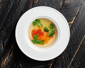 broccoli soup carrot parsley potatoes in a white round plate on a black textured wood background