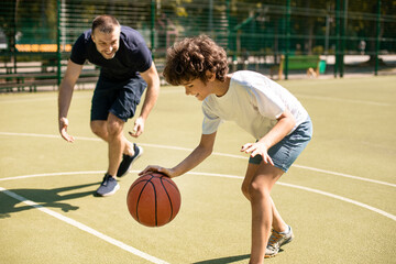Sportive dad teaching his son how to play basketball outside