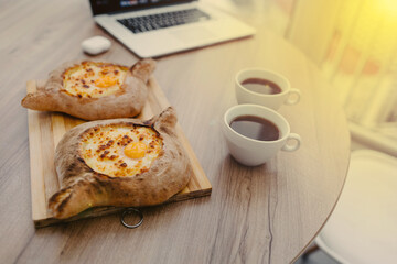 Two khachapuri and two cups of coffee, a dish of georgian cuisine on a wood table in an office