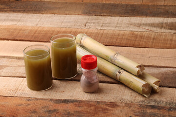 Sugarcane juice in glass with piece of sugarcane and black salt on wooden table 
