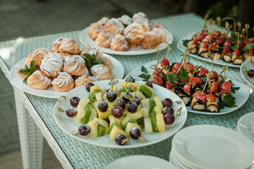 Close-up of a served table with snacks for a festive celebration: sweet desserts (eclair), fruits and other dishes